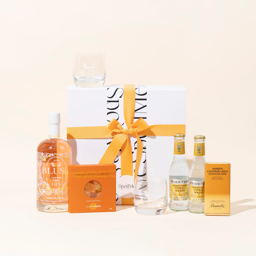 A Gin gift box set with a bottle of Blush citrus pink gin, two gin glasses, a small bottle of tonic, a chocolate bar, and a message card.